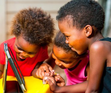 Three young children sharing a tablet together outdoors