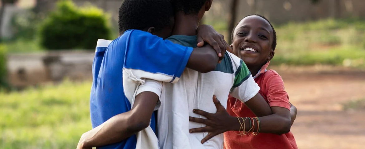Three children embracing outdoors, reflecting the community partnerships behind GOW's work