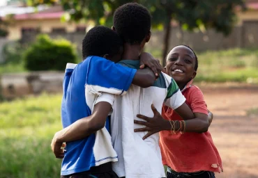 Three children embracing outdoors, reflecting the community partnerships behind GOW's work