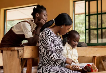 Mentor reading a textbook with two pupils in a classroom during a GOW mentorship session