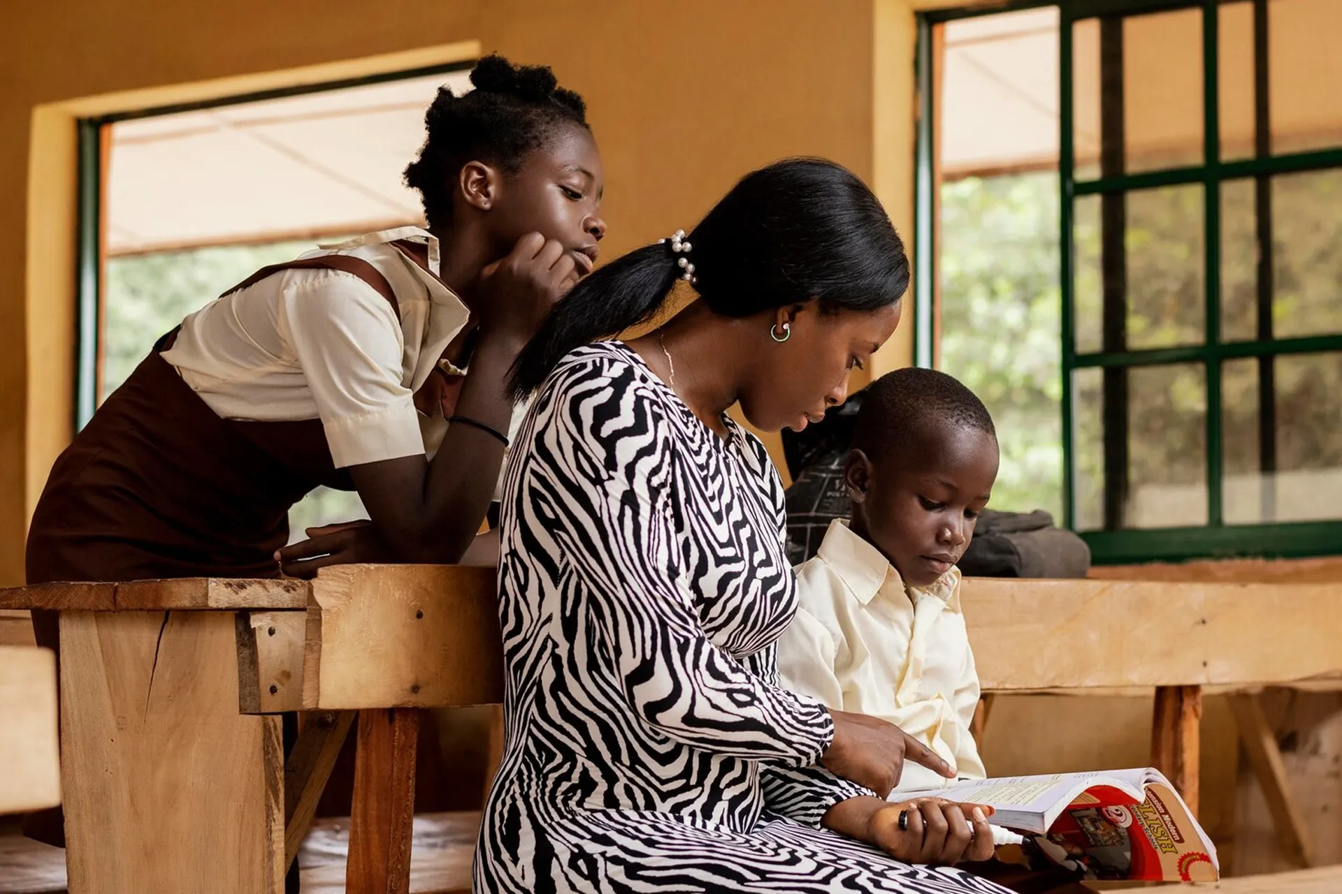 Mentor reading a textbook with two pupils in a classroom during a GOW mentorship session
