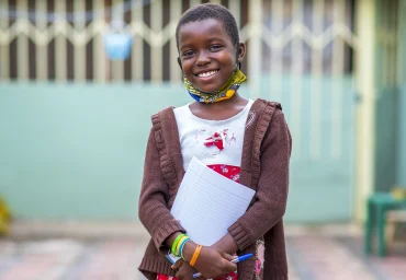 Smiling schoolgirl holding her exercise book, supported by Oloowere Foundation tuition assistance